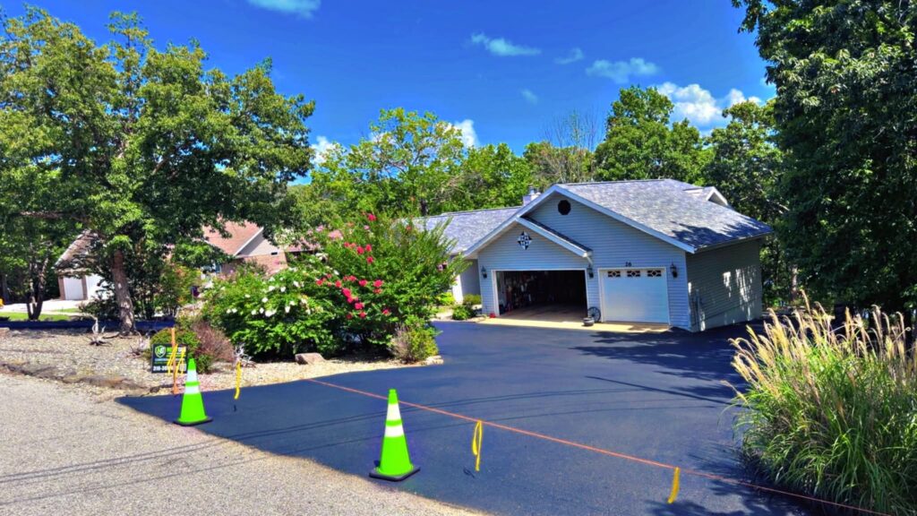 Freshly sealcoated residential driveway with cones and protected landscaping