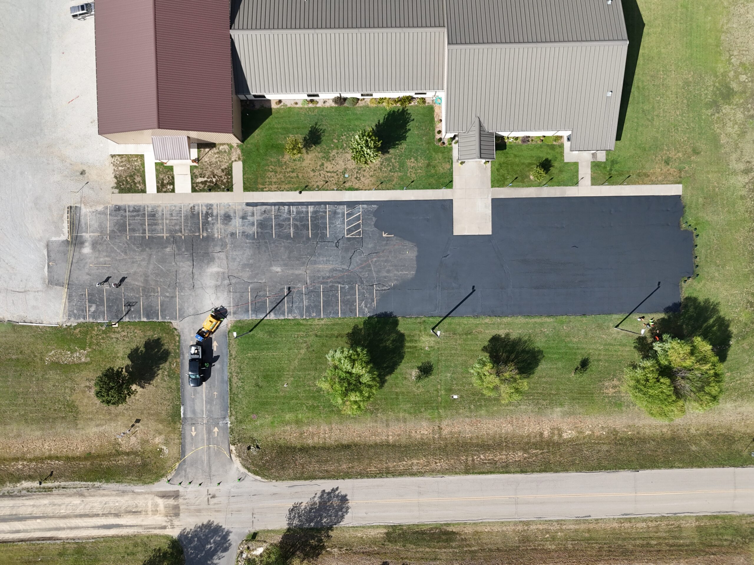 Sealcoating underway at Freedom Church, with one side coated and treated cracks visible on the remaining surface