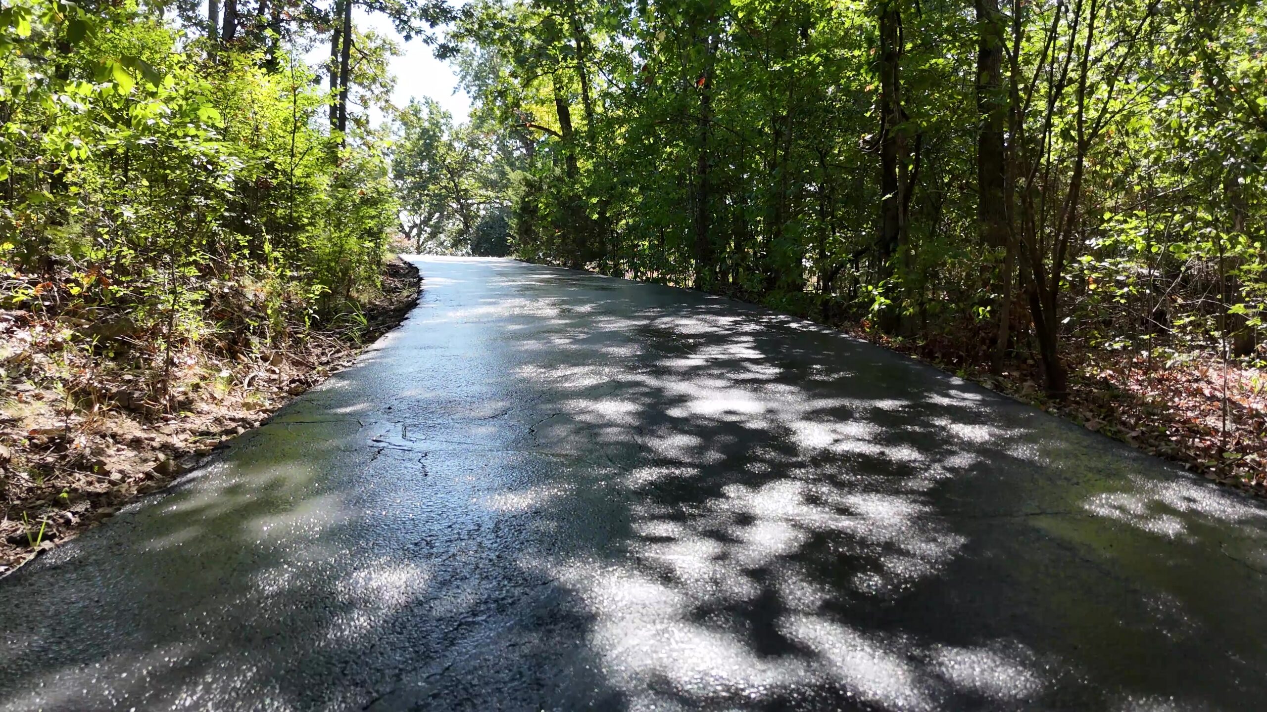 Freshly coated uphill driveway beside a rocky bank and trees in Lampe