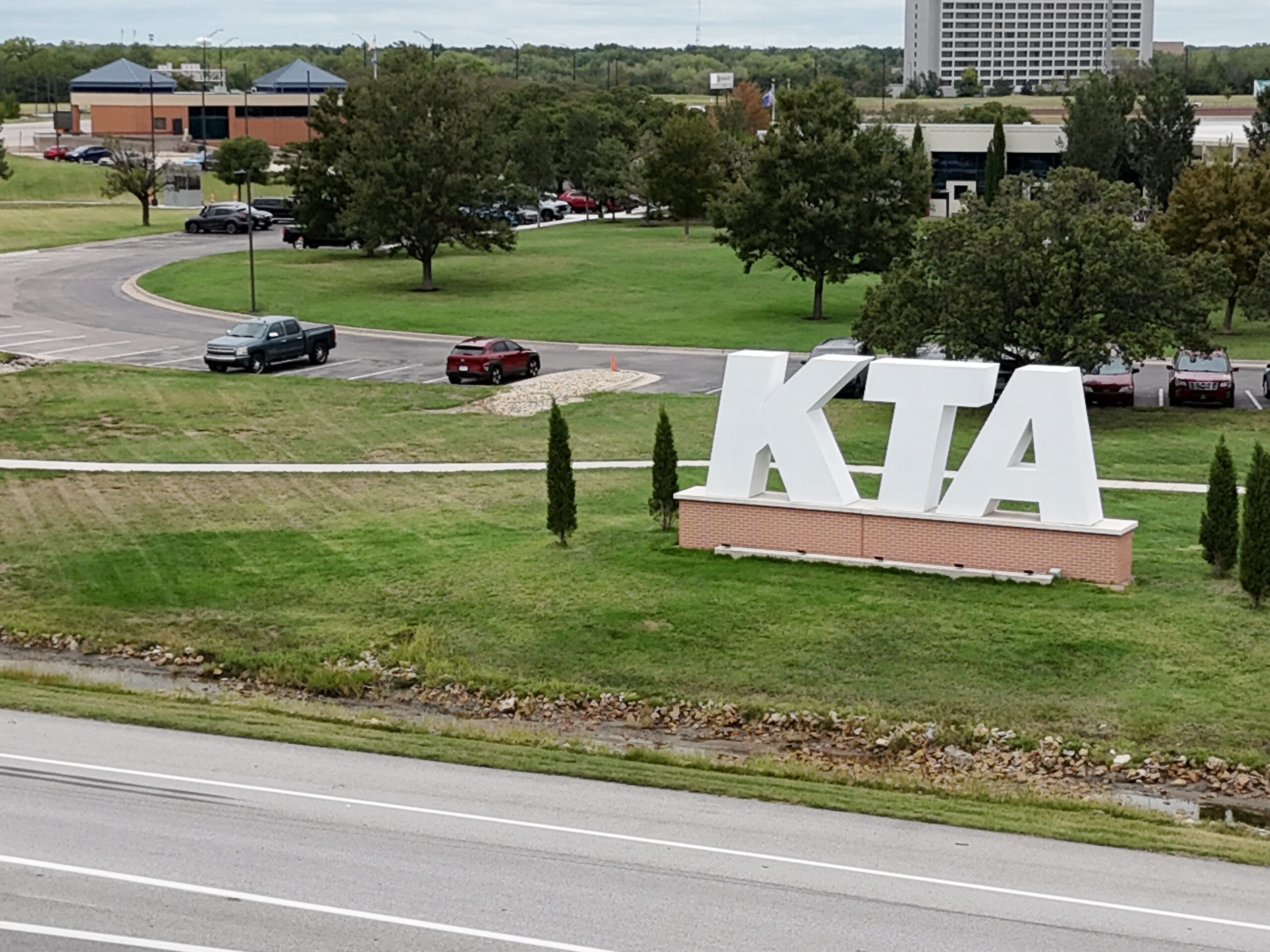 Large white KTA letters at the Wichita headquarters entrance, with the campus behind them, photographed September 21 before sealcoating