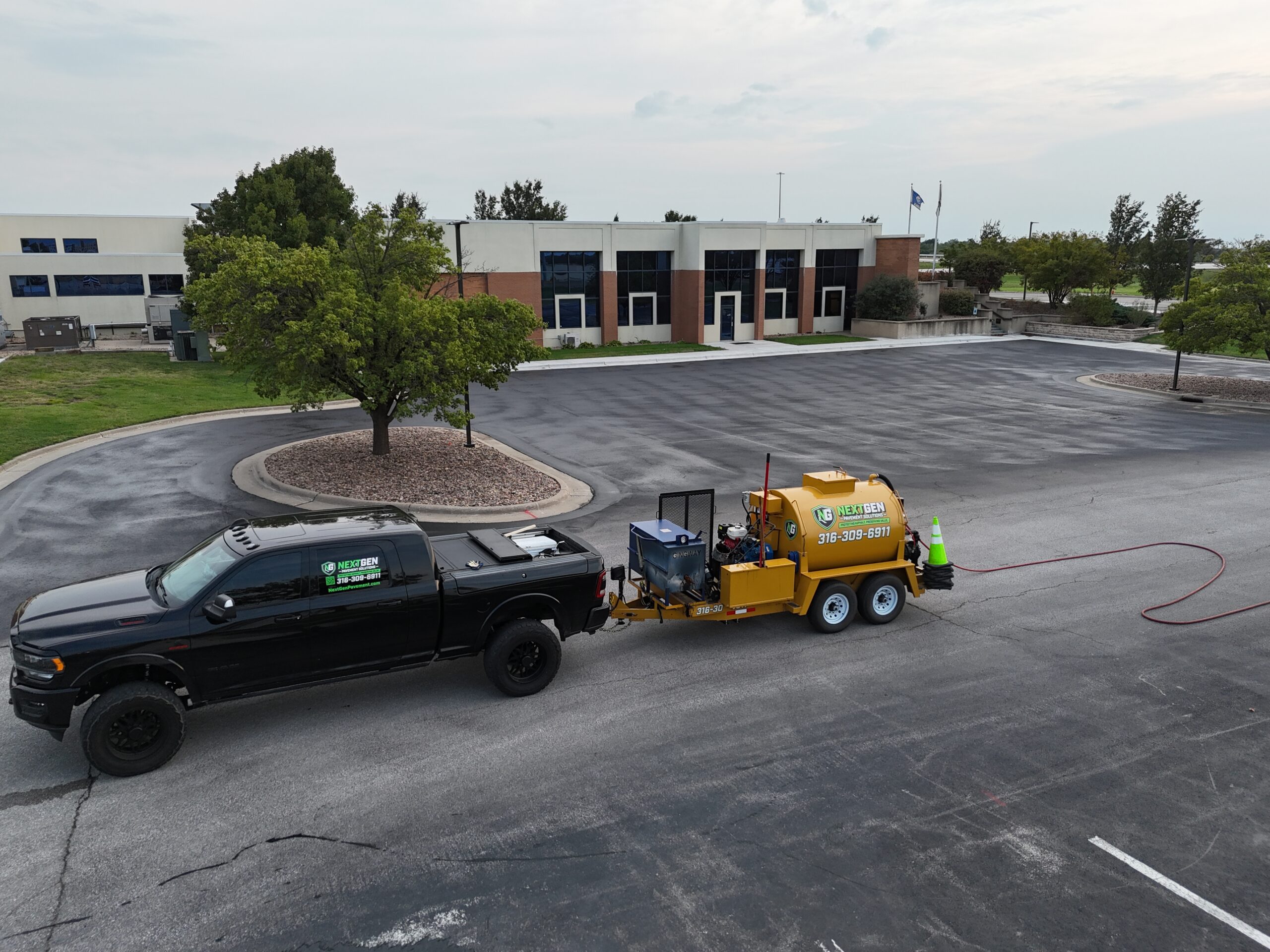 KTA Wichita Headquarters Sealcoating NextGen-branded truck and yellow sealcoating trailer in front of the KTA headquarters building