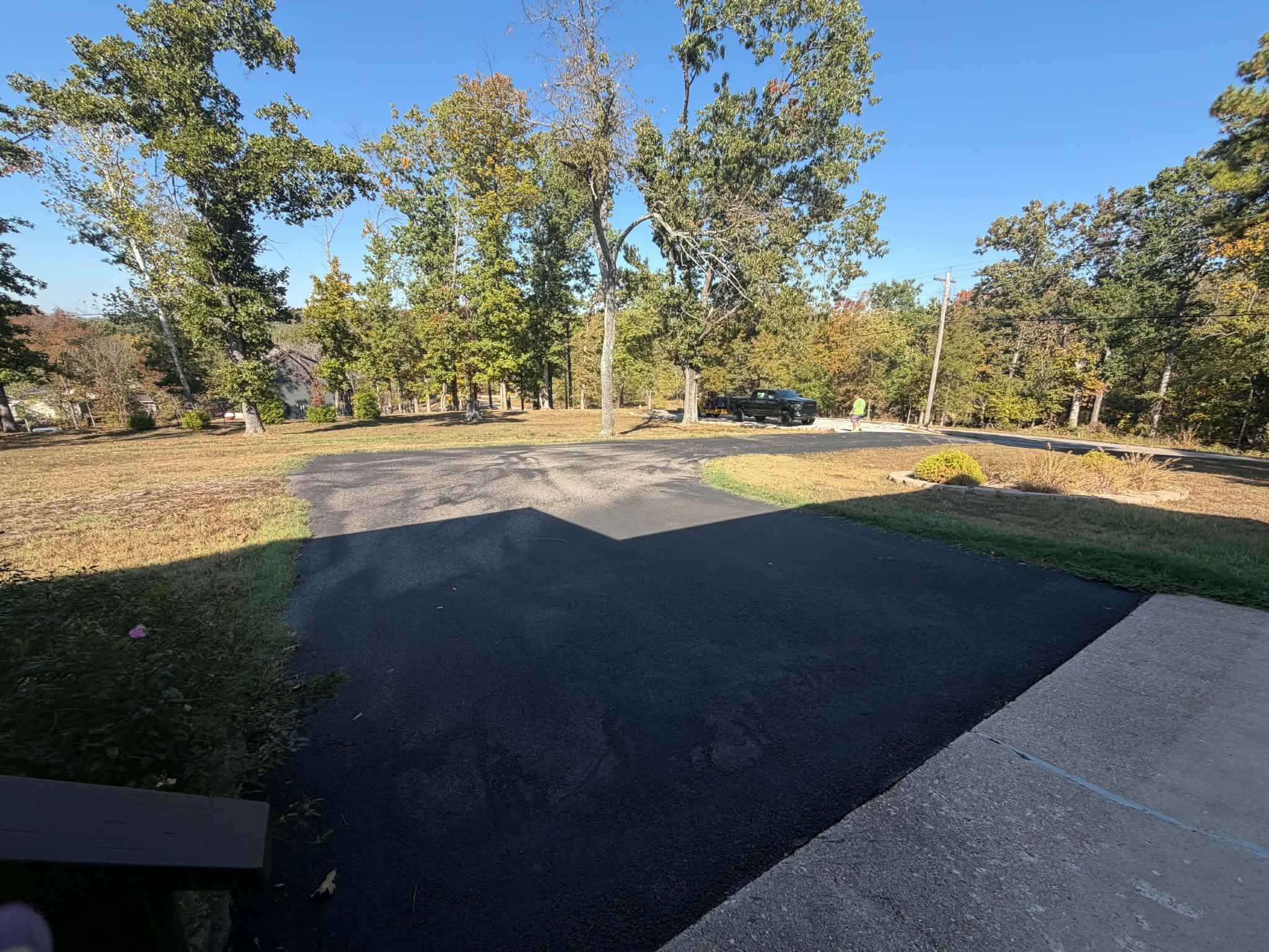 Ground-level view of the freshly sealcoated driveway curving through a wooded Cape Fair property.