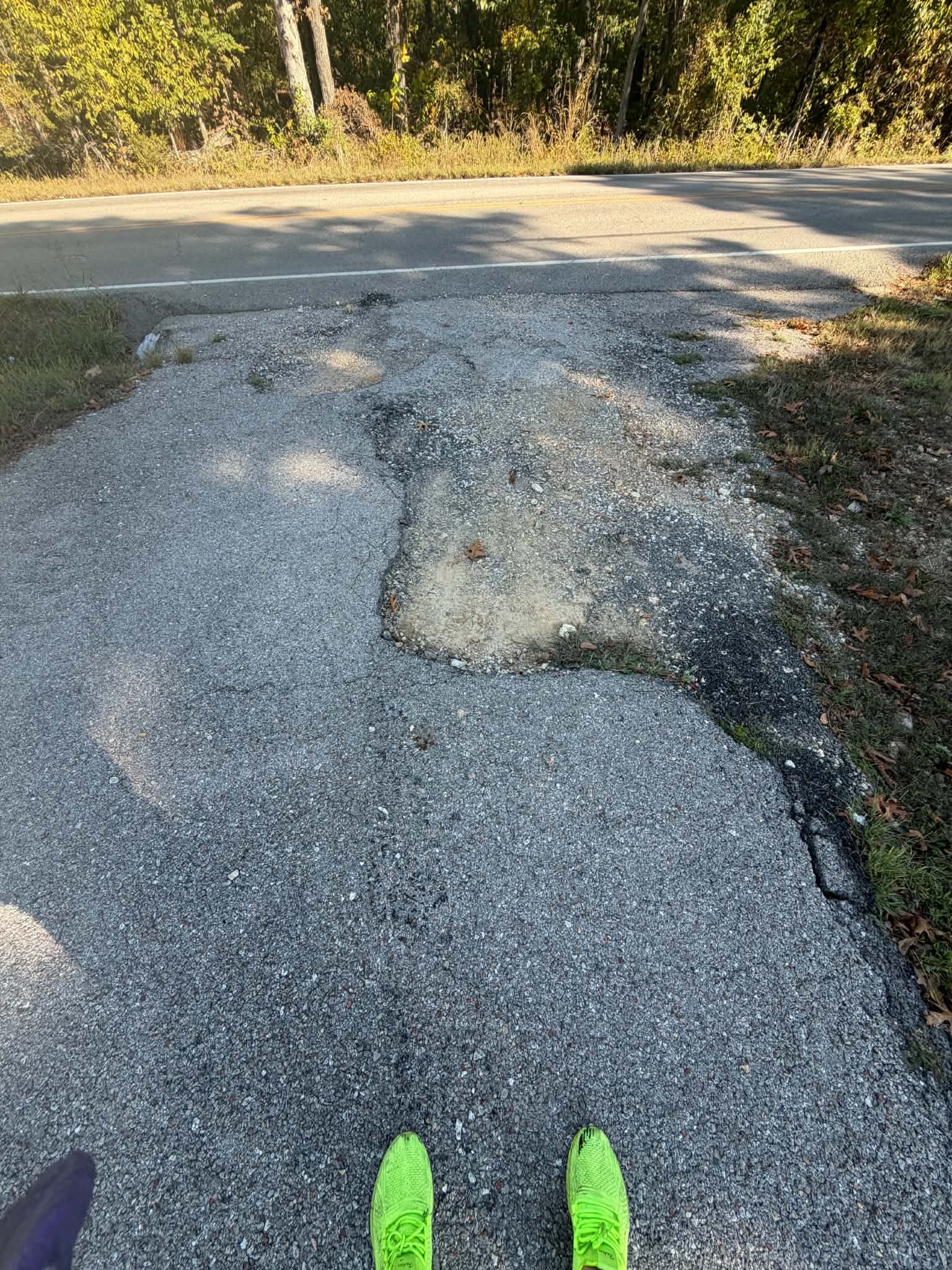 Broken asphalt edges and deteriorated spots at the driveway approach before localized maintenance.